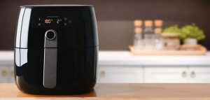 Black digital air fryer placed on a wooden kitchen counter with a blurred background.