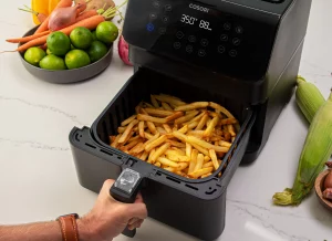Air fryer with hot crispy French fries ready to serve on kitchen counter.