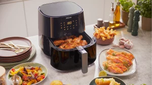 Modern air fryer cooking chicken drumsticks surrounded by healthy, freshly prepared meals on a kitchen counter.