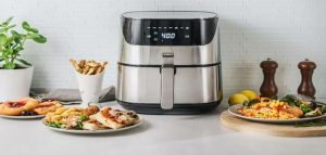 Stainless steel air fryer surrounded by assorted cooked meals on a kitchen counter.