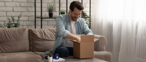 Happy man opening a delivery box at home on a couch