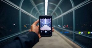 Person taking a photo of a modern pedestrian bridge at night using a smartphone.