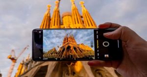 Person holding a smartphone capturing the iconic Sagrada Familia cathedral in Barcelona at sunset.