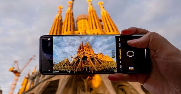 Person holding a smartphone capturing the iconic Sagrada Familia cathedral in Barcelona at sunset.