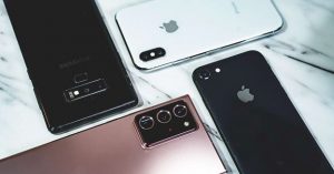 Flat lay of various iPhone and Samsung Galaxy smartphones on a marble surface.