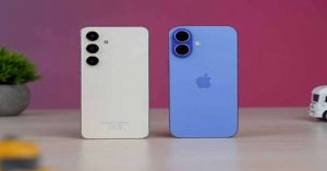 Rear view of a white Samsung smartphone and a blue iPhone on a wooden desk with a pink background.