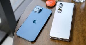 Close-up of a blue iPhone and a white Samsung Galaxy Z Fold smartphone placed on a wooden table.