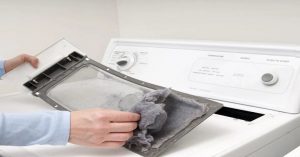 Person cleaning the lint filter of a white dryer machine to maintain efficiency and safety.
