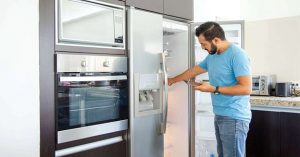 Man in kitchen checking refrigerator, modern appliances, simple kitchen layout. 