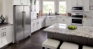 a bright, modern kitchen featuring white cabinetry, stainless steel appliances, and a spacious island with a granite countertop. 