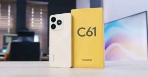 Realme C61 smartphone in cream color with its yellow retail box displayed on a desk.