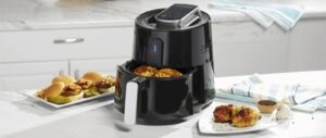 Black air fryer with cooked chicken and sliders on a kitchen counter.