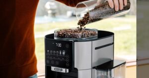 Person pouring coffee beans into DeLonghi espresso machine grinder.