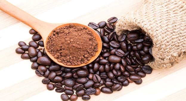 Ground coffee on wooden spoon with scattered roasted beans and burlap sack