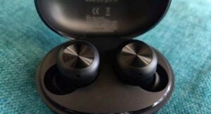 Black wireless earbuds in open charging case on blue fabric surface.

