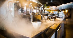 Professional espresso machine brewing coffee in a steamy café environment.