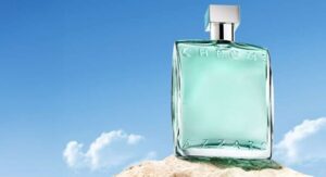 Chrome Azzaro perfume bottle with a light blue liquid placed on a rock against a clear blue sky