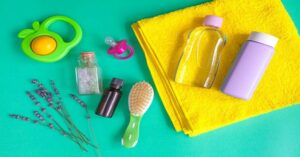 Baby bath essentials including towel, brush, pacifier, lotion, and lavender on green background. 