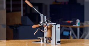 Manual lever espresso machine with wooden handles on a workbench.