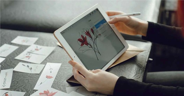 Drawing a flower on tablet using stylus with sketches on table
