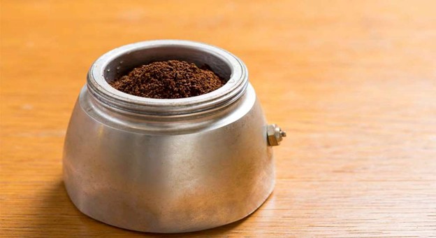 Ground coffee in moka pot filter on wooden surface