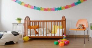 Wooden baby crib in colorful nursery with toys, chair, and wall decorations. 