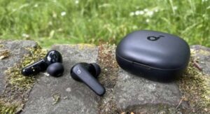 Black wireless earbuds and case resting on a stone surface outdoors.