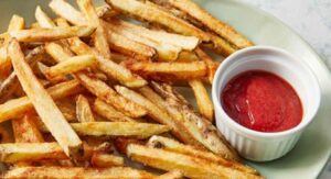 Crispy French fries served with ketchup in a white ramekin.