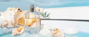 Clear perfume bottle with seashells and white stones by a poolside. 