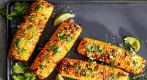 Grilled corn on the cob with herbs and lime wedges.