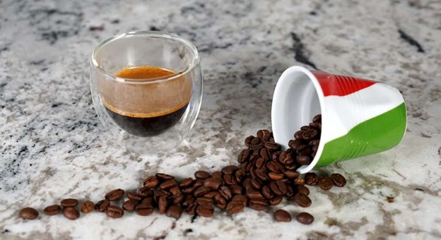 Espresso in glass cup with spilled coffee beans and Italian flag cup on marble