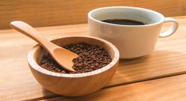 Wooden bowl of instant coffee with spoon and white coffee cup