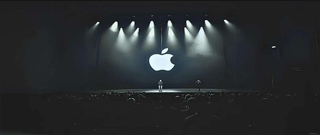 Apple keynote stage with large logo and spotlight presentation