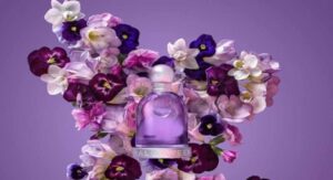 Halloween perfume bottle surrounded by vibrant purple and white flowers on a purple background. 