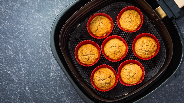 Baked muffins in red silicone cups inside an air fryer basket.