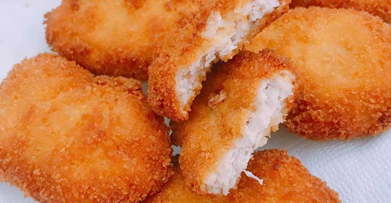 Crispy golden chicken nuggets with a juicy inside on white background.

