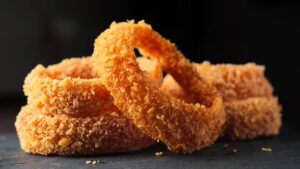 Crispy golden onion rings stacked on dark surface.