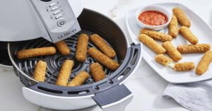 Mozzarella sticks cooked in air fryer with dipping sauce on side plate.
