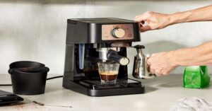 Person using a home espresso machine to brew coffee into a glass cup.