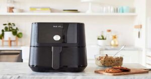 Black air fryer on kitchen counter with cookie dough and baked cookies. 