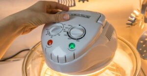 Hand adjusting temperature dial on a convection oven lid with indicator lights.