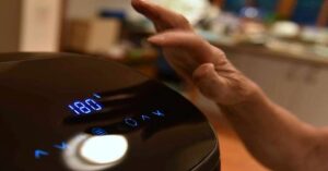 Hand adjusting digital air fryer temperature set to 180 degrees. 