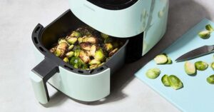 Roasted Brussels sprouts in air fryer basket beside cutting board with fresh sprouts.