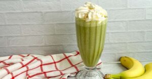 Glass of matcha banana smoothie topped with whipped cream beside fresh bananas