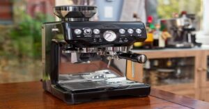 Black Breville espresso machine with built-in grinder on a wooden kitchen counter.