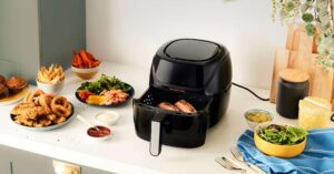 Air fryer on kitchen counter surrounded by various cooked foods and dipping sauces.
