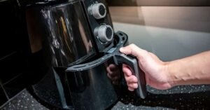 Hand pulling out an air fryer basket from a black kitchen appliance.