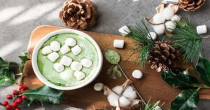 Festive matcha latte topped with marshmallows, surrounded by pine cones and holiday decorations.
