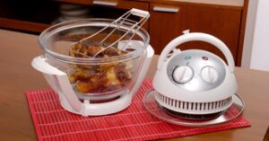 Cooked chicken in glass convection oven with detached control lid on red placemat.