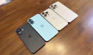Four iPhones in different colors placed on a wooden surface.

